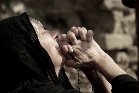 anziana con un velo nero prega tenendo un rosario tra le mani giunte